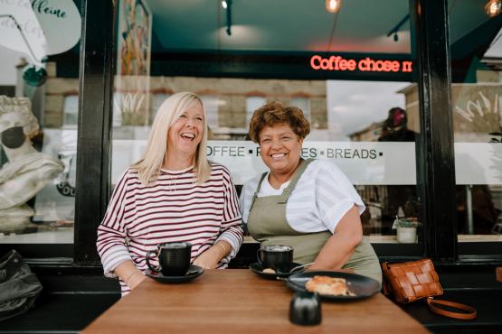 Two ladies sitting outside a coffee shop chatting and laughing
