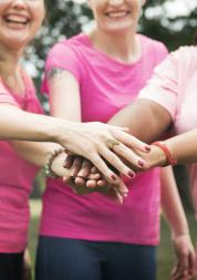 Four women wearing pink t-shirts holding one hand of top of another