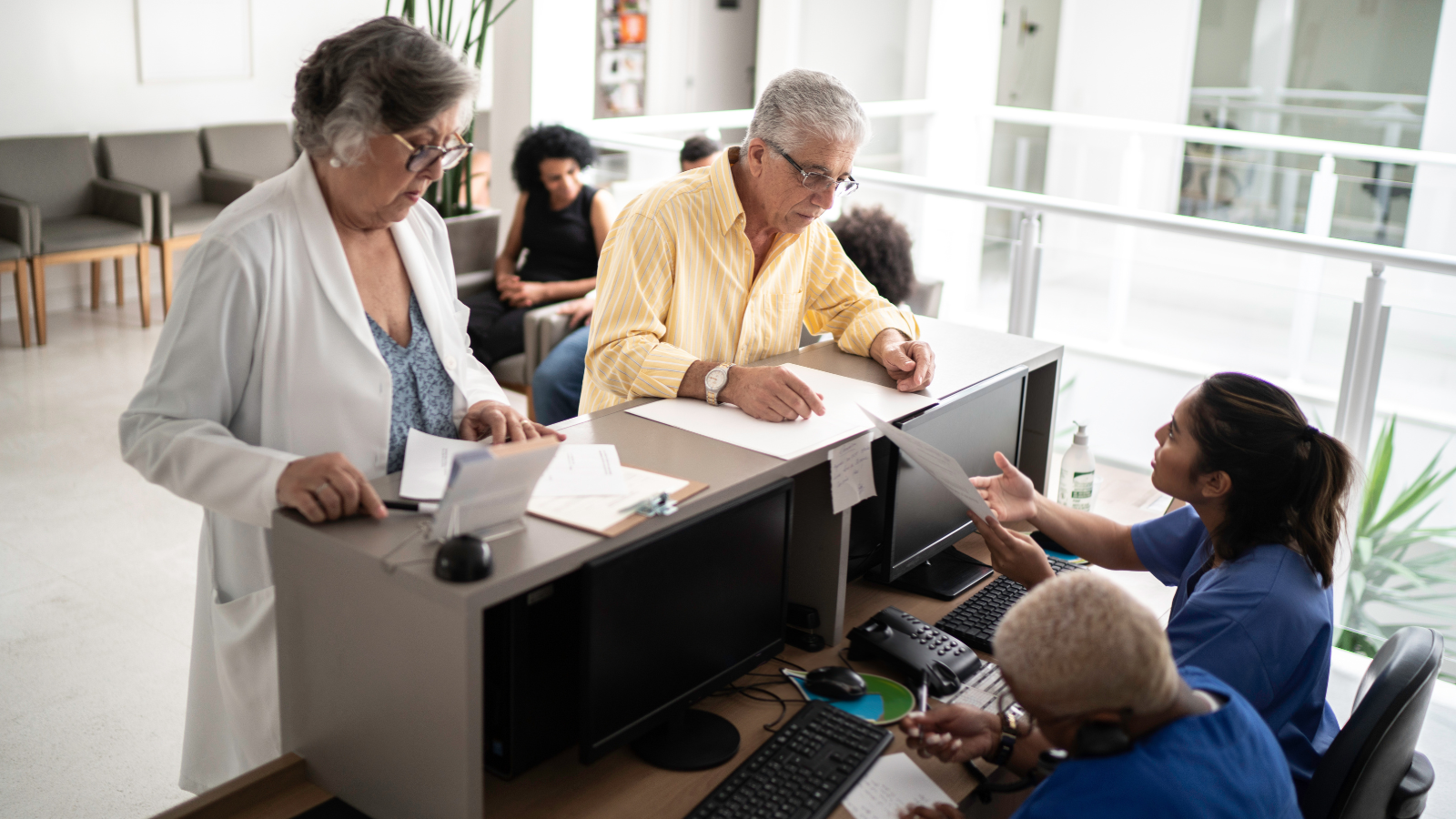 Two adults talking to reception staff who are behind a desk sitting down