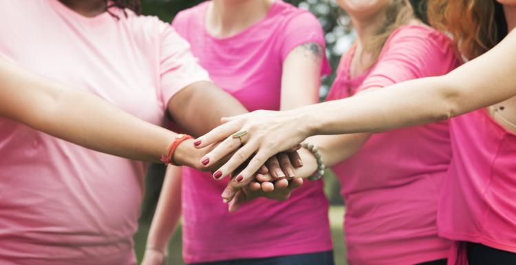 Four women wearing pink t-shirts holding hands on top of each other