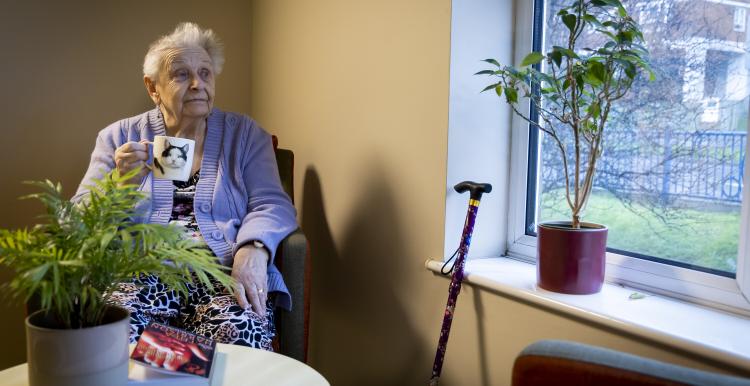 Senior lady sitting in a chair, having a hot drink and looking out of the window