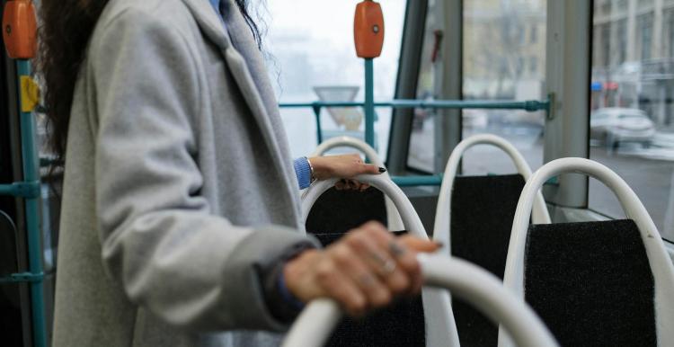 Image of a lady standing on a bus holding the bus seats