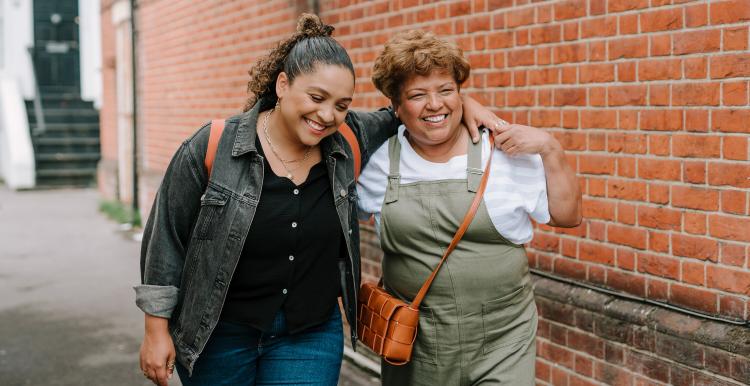 Two ladies walking down a street holding each other and smiling 