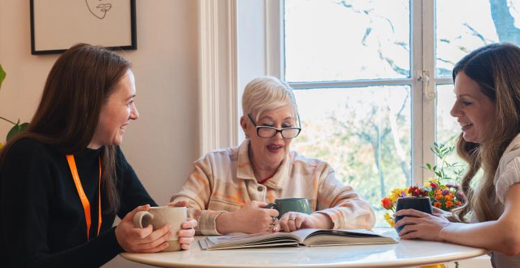 Three people sitting around a table enjoying a hot drink and chatting