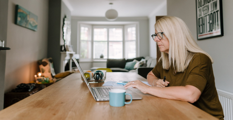 Lady sitting at the table in her lounge with a hot drink and a laptop