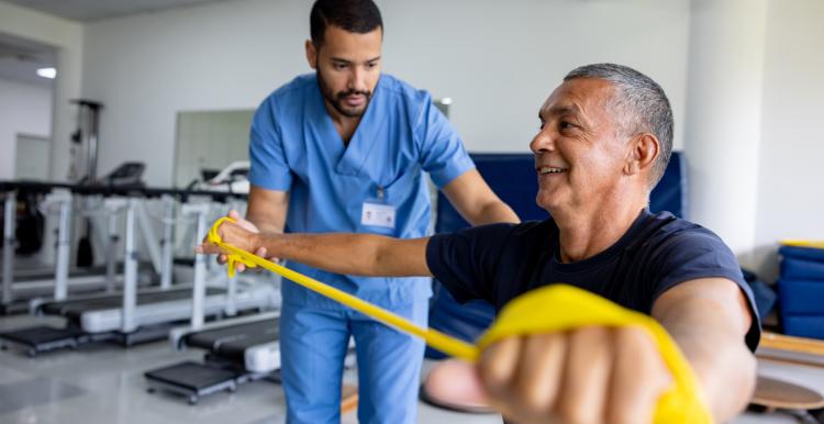 Mature man doing physical therapy exercises using a stretch band with the assistance of his therapist