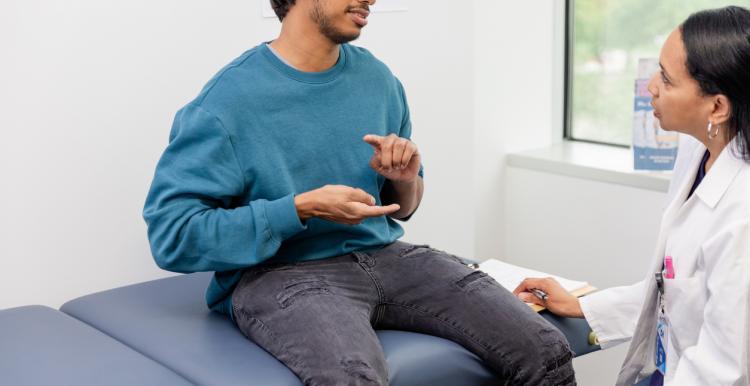 Male patient sitting on a bed signing to a doctor