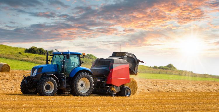 Tractor preparing of straw millstones in a field with sunlight during August