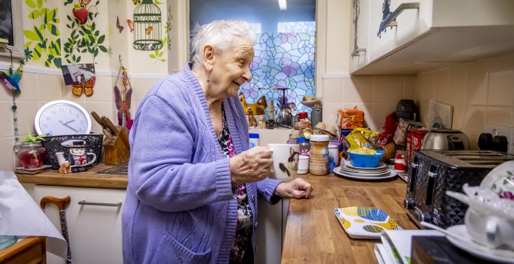 Older lady holding a cup of tea in her kitchen