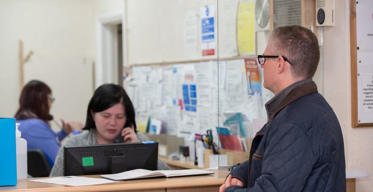 Man waiting at GP reception with receptionist on the phone