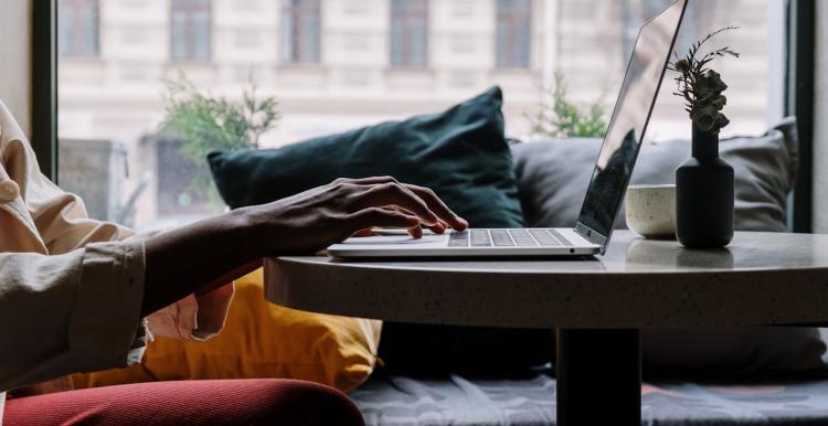 Person using a laptop in a cafe on a small table while seated