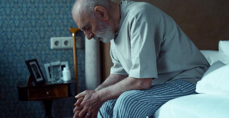 Sad elderly man sitting on his bed