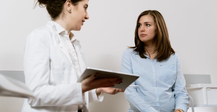 A doctor talking to a lady who's sitting on a bed in a doctors room