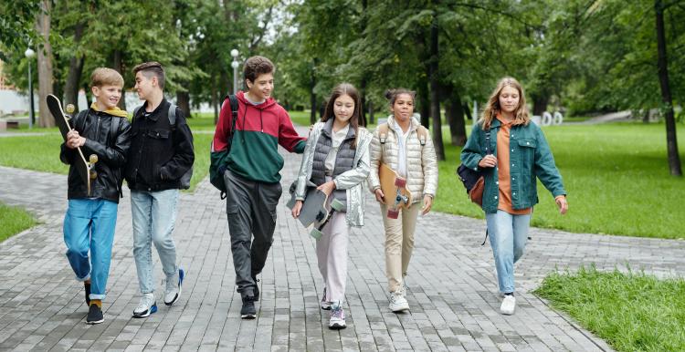 Group of teenagers walking in a line chatting and smiling through a park
