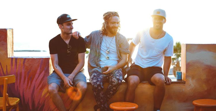 3 men sitting on a wall chatting