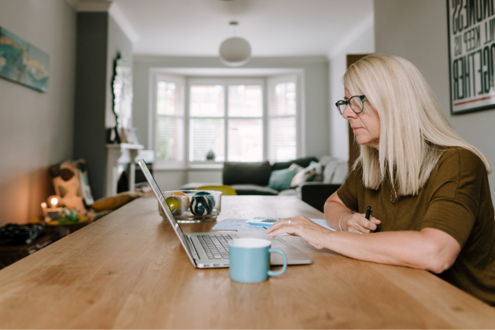 Lady sitting at the table in her lounge with a hot drink and a laptop