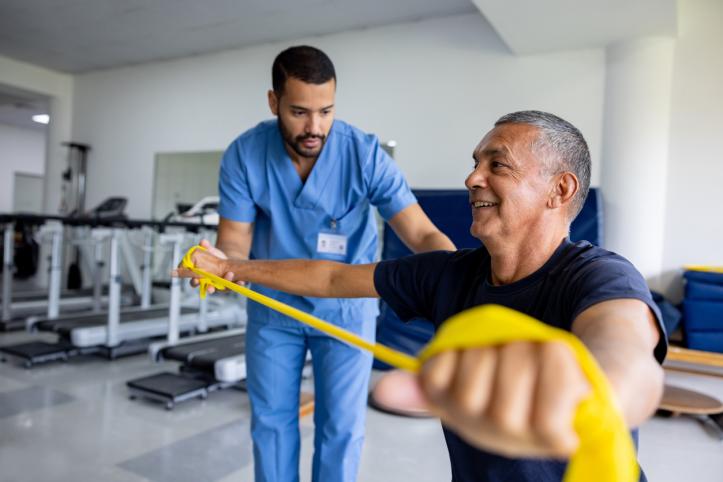 Mature man doing physical therapy exercises using a stretch band with the assistance of his therapist