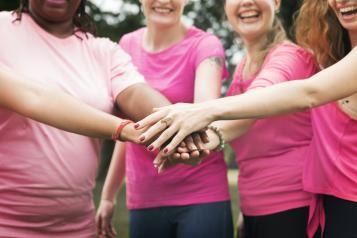 Four women wearing pink t-shirts holding hands on top of each other