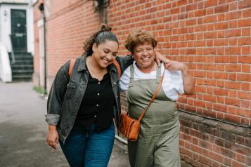 Two ladies walking down a street holding each other and smiling 