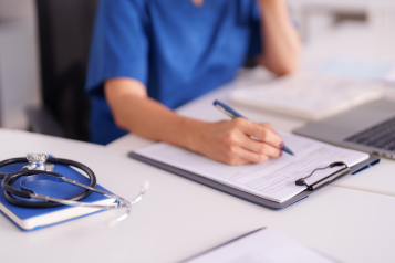 A medical staff member filling out of a form while sitting at her desk