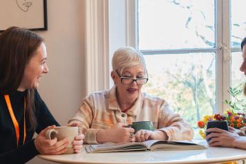 Three people sitting around a table enjoying a hot drink and chatting