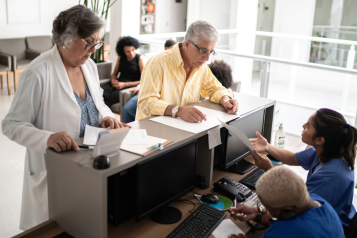 Two adults talking to reception staff who are behind a desk sitting down