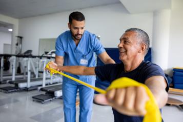 Mature man doing physical therapy exercises using a stretch band with the assistance of his therapist