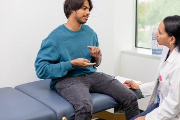 Male patient sitting on a bed signing to a doctor