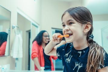 Young girl brushing her teeth in the bathroom with parental supervision, promoting healthy dental habits.