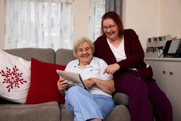 Two ladies sitting on a couch reading the newspaper