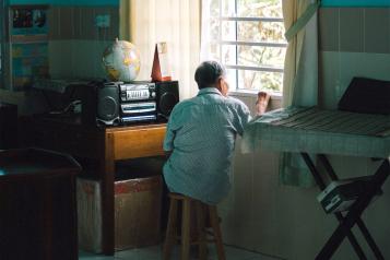An elderly man looks out a window in the afternoon.
