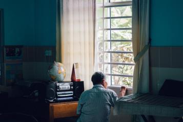 An elderly man looks out a window in the afternoon