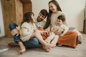 Family with parents and 2 children playing on the floor and smiling