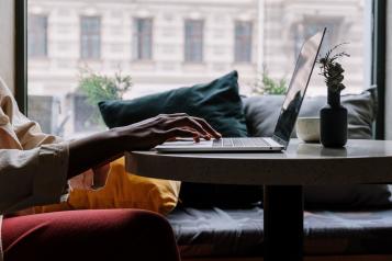 Person using a laptop in a cafe on a small table while seated