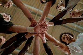 Group of people in a circle each with a hand of top of each other