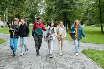Group of teenagers walking in a line chatting and smiling through a park