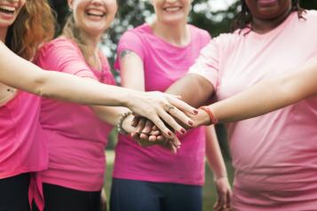 Four women wearing pink t-shirts holding one hand of top of another