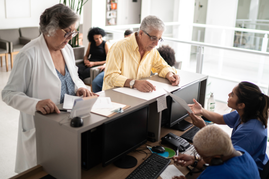 Two adults talking to reception staff who are behind a desk sitting down