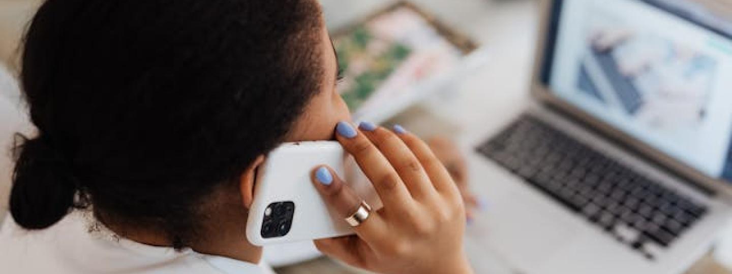 Lady talking on her mobile phone, sitting at her desk with her laptop open