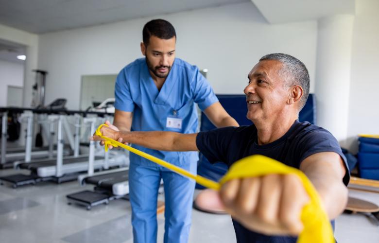 Mature man doing physical therapy exercises using a stretch band with the assistance of his therapist