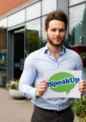 Man holding a sign outside a hospital that says 'Speak Up' 