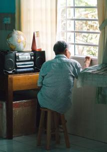 An elderly man looks out a window in the afternoon.